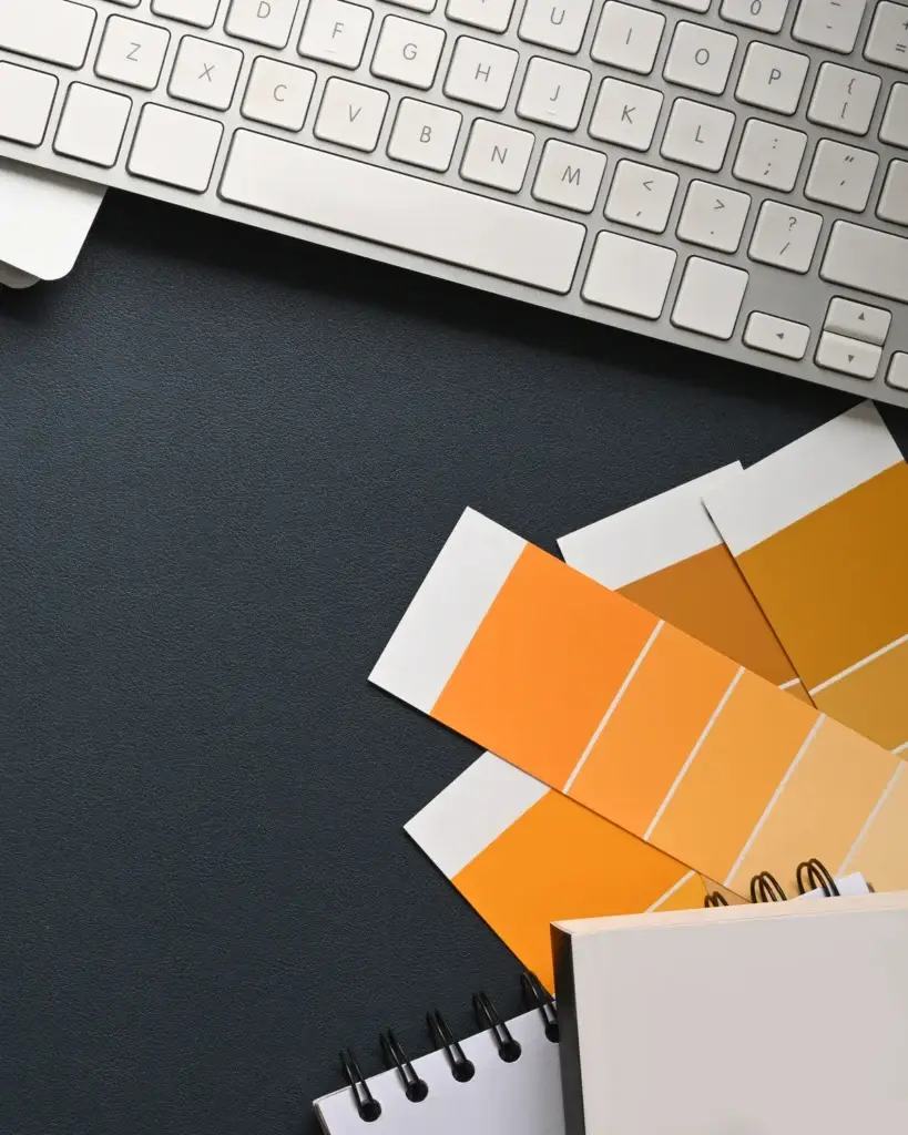 Designer’s desk with keyboard, colour swatches and notebooks on a dark surface