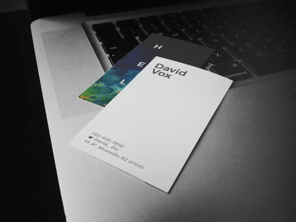David Vox business cards, white front and a marbled blue-green back, on a laptop